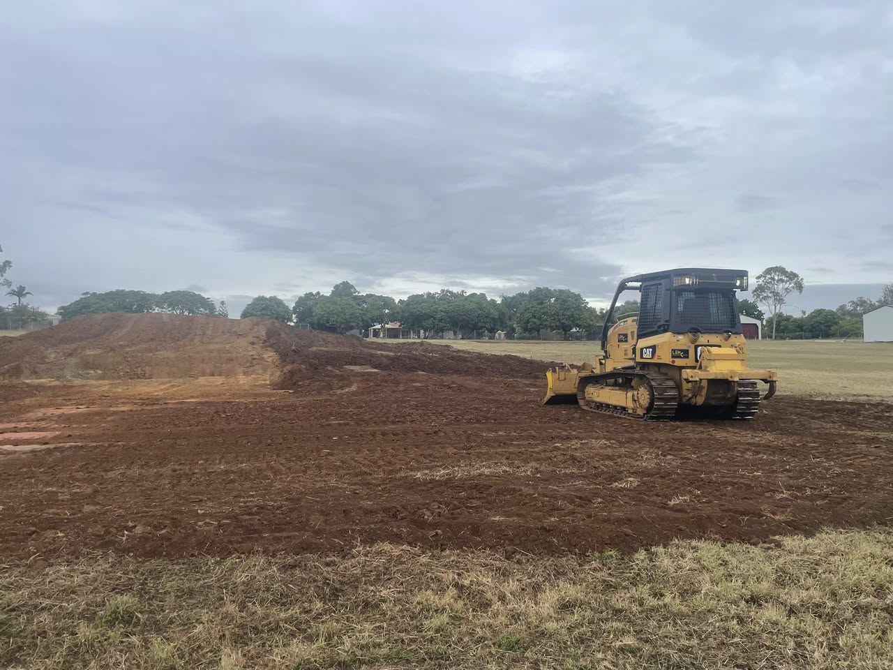 Dozer on a graded sports oval with a long row of red-dirt mound behind
