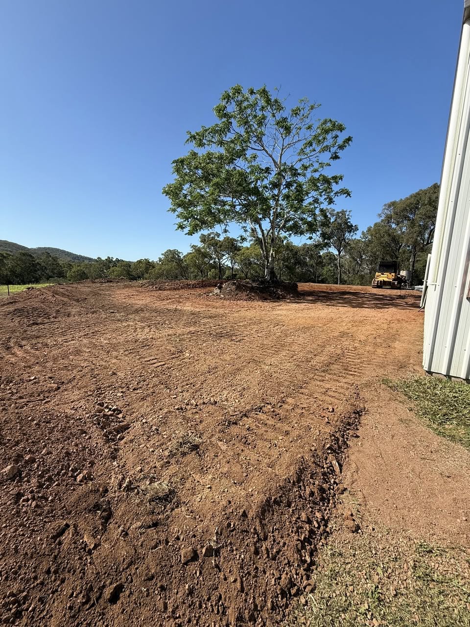 Freshly graded red-dirt pad with hills and a single gum tree in the background