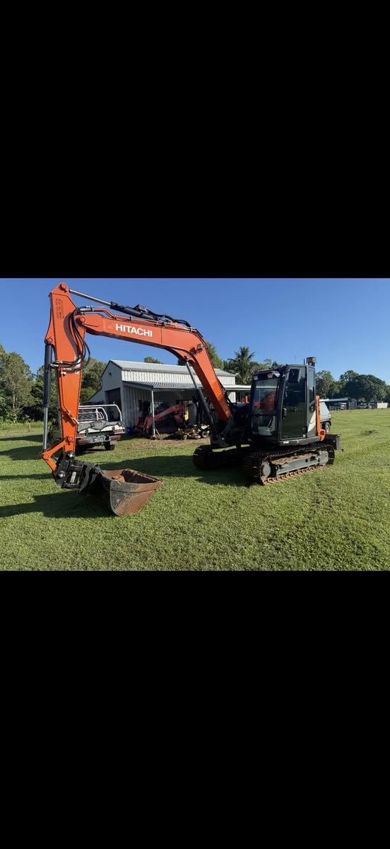 Hitachi excavator with bucket lowered on a green lawn next to a workshop